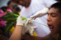 PHUKET, THAILAND - OCTOBER 05: A devotee of the Chinese shrine of Sui Boon Tong Shrine, pierces his cheeks with rubber tube during a procession of Vegetarian Festival on October 5, 2011 in Phuket, Thailand. Ritual Vegetarianism in Phuket Island traces it roots back to the early 1800's. The festival begins on the first evening of the ninth lunar month and lasts for nine days. Participants in the festival perform acts of body piercing as a means of shifting evil spirits from individuals onto themselves and bring the community good luck. (Photo by Athit Perawongmetha/Getty Images)