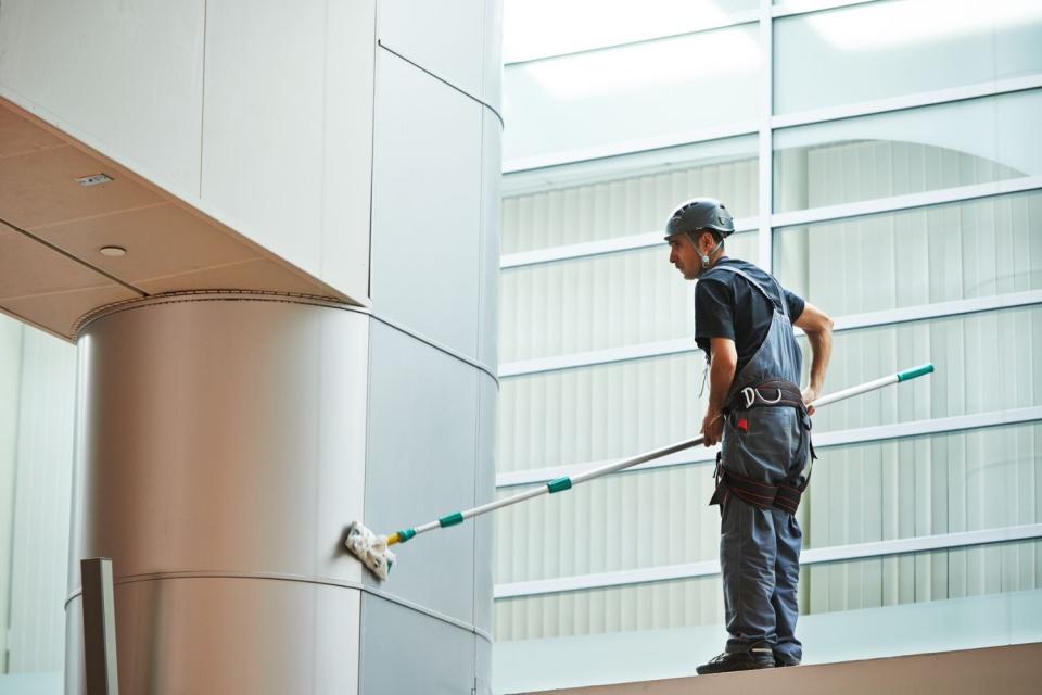 A cleaner uses a tool to clean the walls inside a large hall.