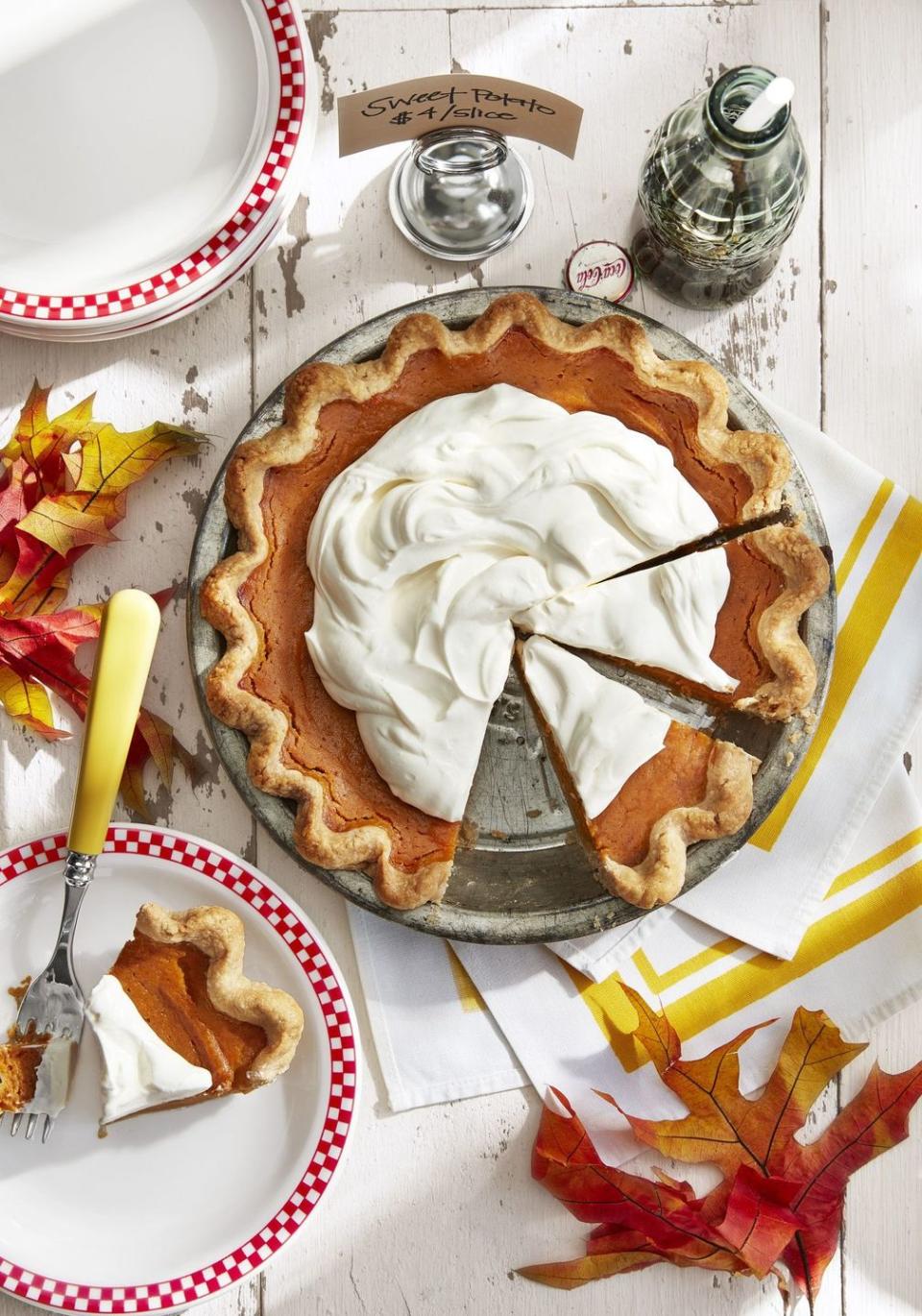 gingery sweet potato pie topped with whipped cream in a metal pie dish with a slice on a plate next to it