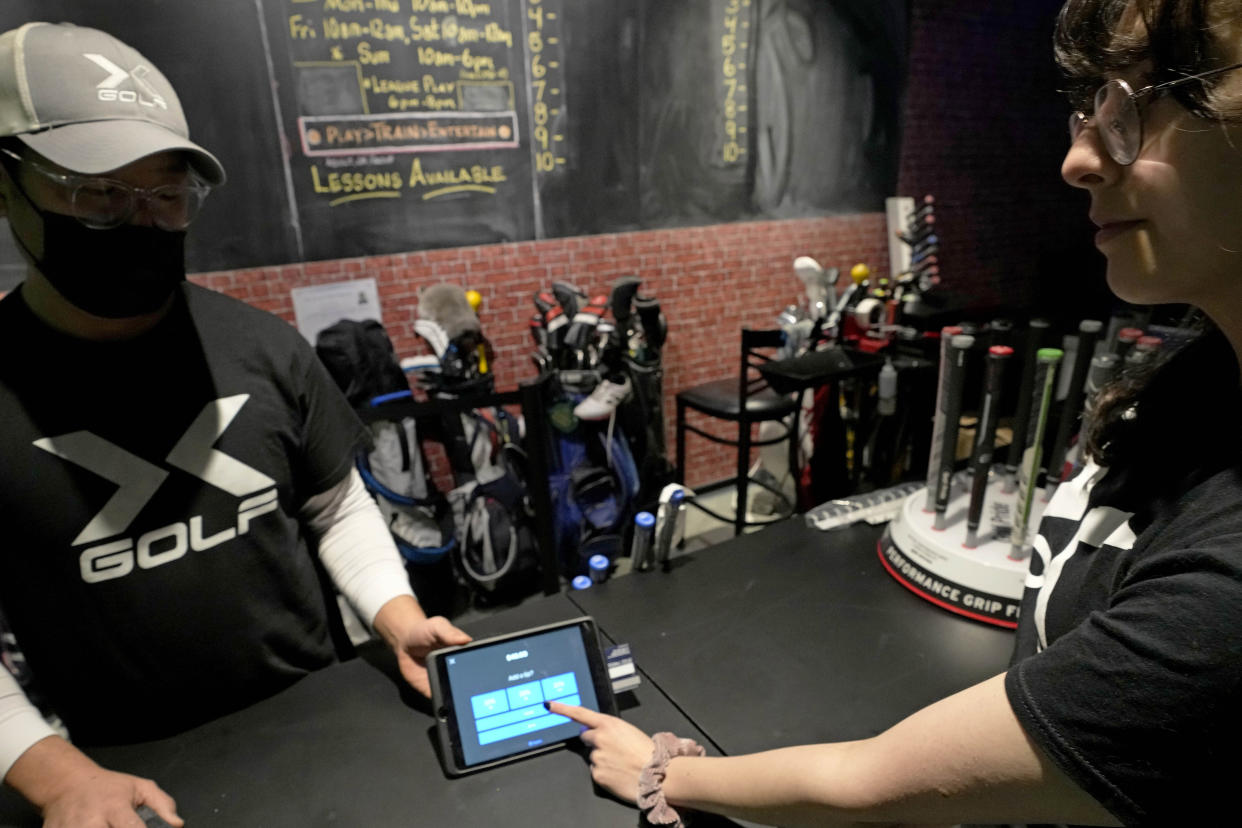 X-Golf manager J.W. Park, left, helps Ashley Moreno to check out at X-Golf indoor golf in Glenview, Ill., Friday, Jan. 20, 2023. Tipping fatigue, it seems, is swarming America as more businesses adopt digital payment methods that automatically prompts customers to leave a gratuity. (AP Photo/Nam Y. Huh)