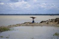 A person carries a corrugated sheet to shift their house because of erosion due to the Meghna River in the Ramdaspur village in the Bhola district of Bangladesh on July 5, 2022. Mohammad Jewel and Arzu Begum were forced to flee the area last year when the river flooded and destroyed their home. (AP Photo/Mahmud Hossain Opu)