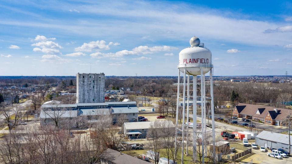 PLAINFIELD, IL, USA - MARCH 19, 2019: A drone / aerial view of a white water tower with Plainfield painted in red with an old grain elevator standing high in the background.