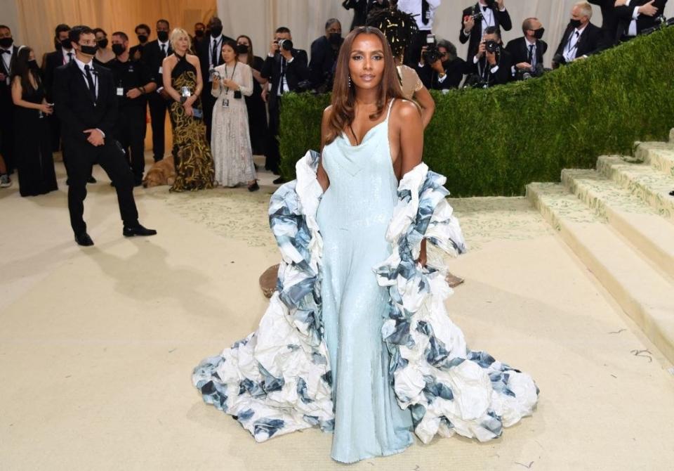 Janet Mock wears a floor length thin strap sparkly gown under a matching ruffle shawl