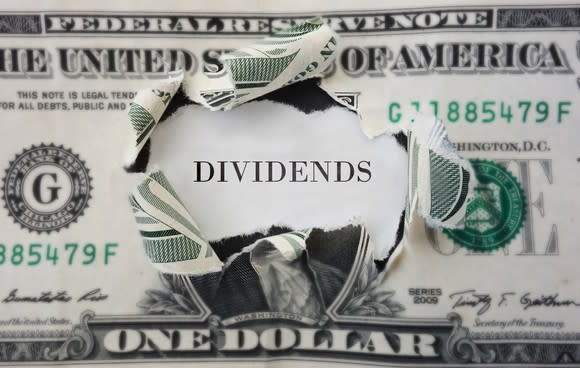 Dollar bill with center torn out and the word "dividends" showing through. 