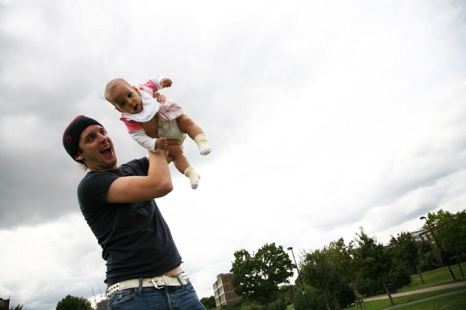 Un padre jugando sosteniendo a su bebé en un parque