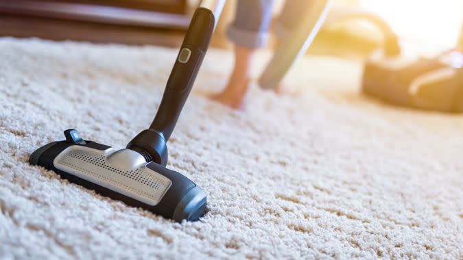 Young woman using a vacuum cleaner while cleaning carpet in the house.