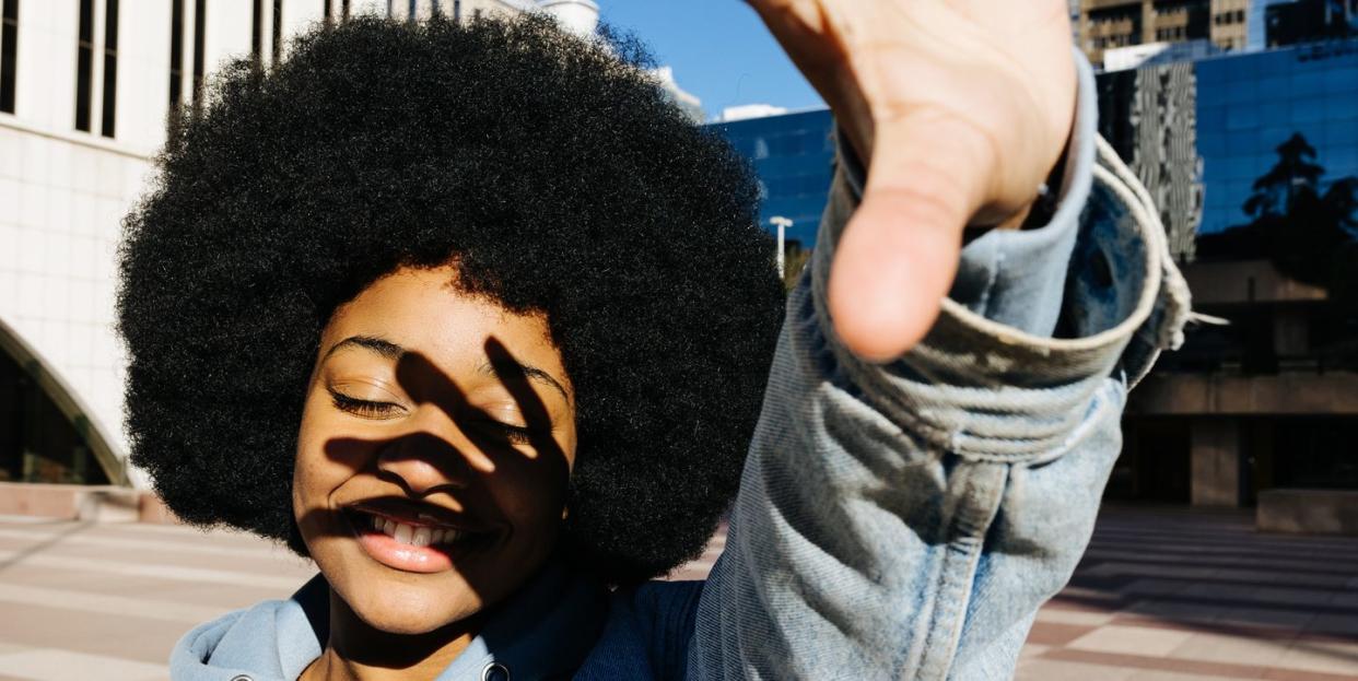 young afro woman with her eyes closed and smiling while covering herself from the sunlight with her hand