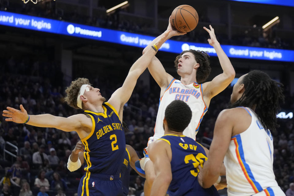 Oklahoma City Thunder guard Josh Giddey, top, shoots against Golden State Warriors guard Brandin Podziemski (2) and guard Stephen Curry, bottom, during the first half of an NBA basketball game in San Francisco, Saturday, Nov. 18, 2023. (AP Photo/Jeff Chiu)