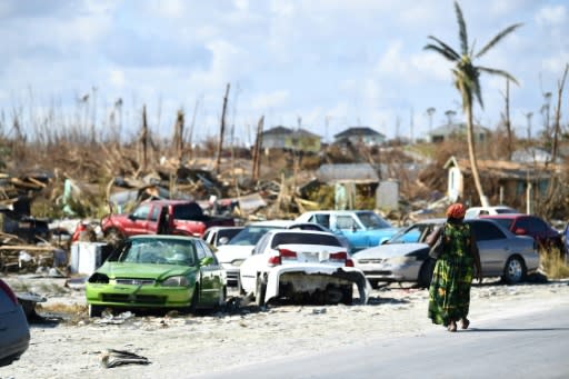 A woman walks by destroyed cars in The Mudd neighborhood of Marsh Harbour