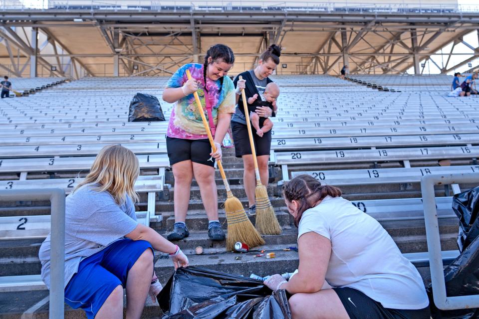 Jazz Compton, from left, Lilly McDole, Kaylynn Young, holding Maverick, Sophi Ricci and other volunteers from Solid Rock Baptist Church (Pendleton), clean up trash in the front straightaway grandstands Monday, May 30, 2022 at the Indianapolis Motor Speedway, the day after the Indianapolis 500 race.