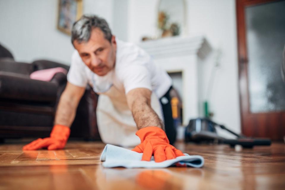 Man wearing rubber gloves, on his knees polishing a wooden floor.