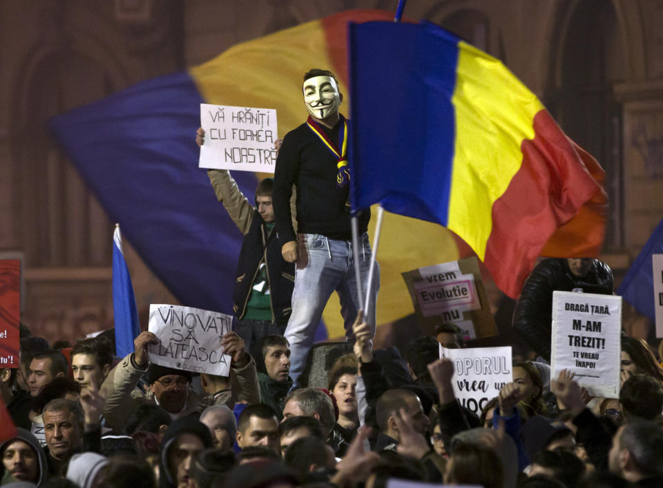 A man wearing a Guy Fawkes mask stands above protesters shouting slogans against the Romanian politicians during the fourth day of protests, joined by tens of thousands across the country, calling for early elections, in Bucharest, Romania, Friday, Nov. 6, 2015. (AP Photo/Vadim Ghirda)