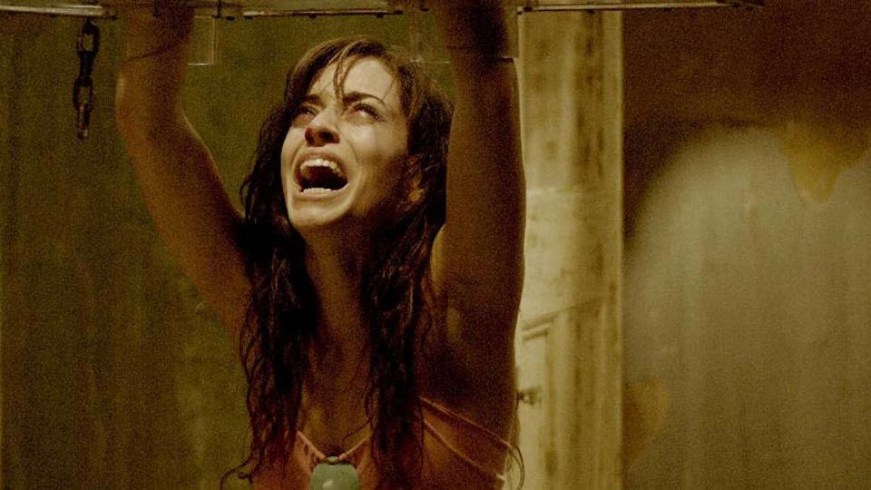 a woman reaches up into a glass jigsaw trap in a scene from saw ii