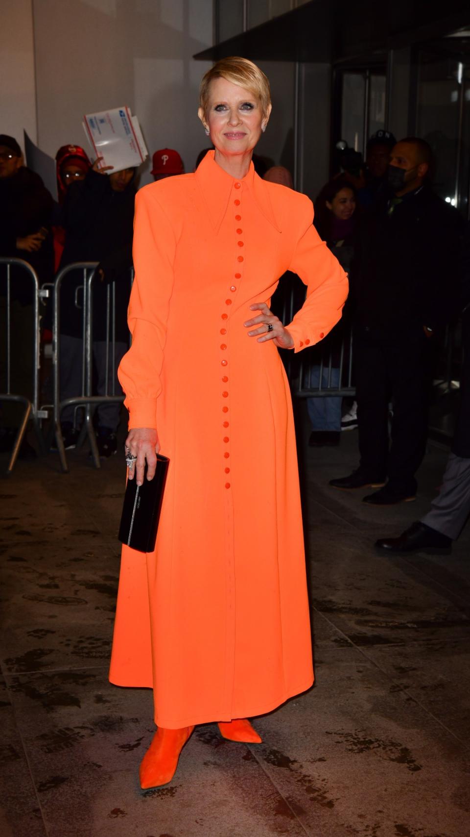 Cynthia Nixon dressed in an orange dress and boots