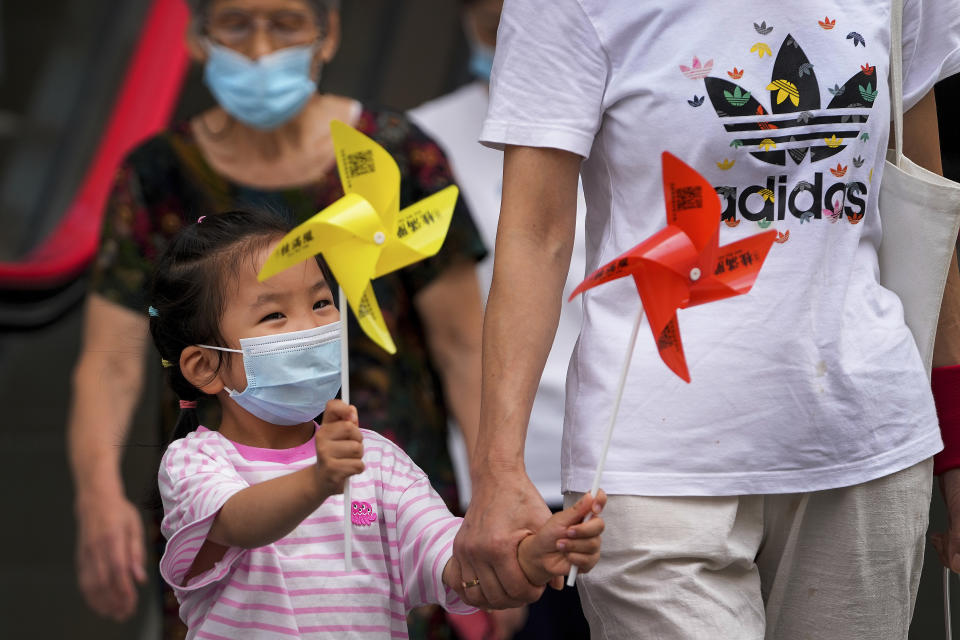 A child wearing a face mask to help curb the spread of the coronavirus holds toy pinwheels as she tour a shopping street with her relatives at the Shanghai Bund in Shanghai, China, Monday, Aug. 23, 2021. (AP Photo/Andy Wong)