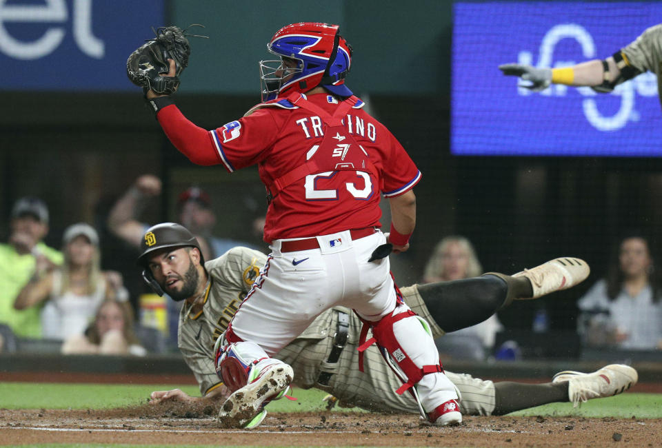 Texas Rangers catcher Jose Trevino (23) looks for the call after San Diego Padres Eric Hosmer (30) slid home during the first inning of a baseball game Friday, April 9, 2021, in Arlington, Texas. Hosmer was ruled safe after a review. (AP Photo/Richard W. Rodriguez)