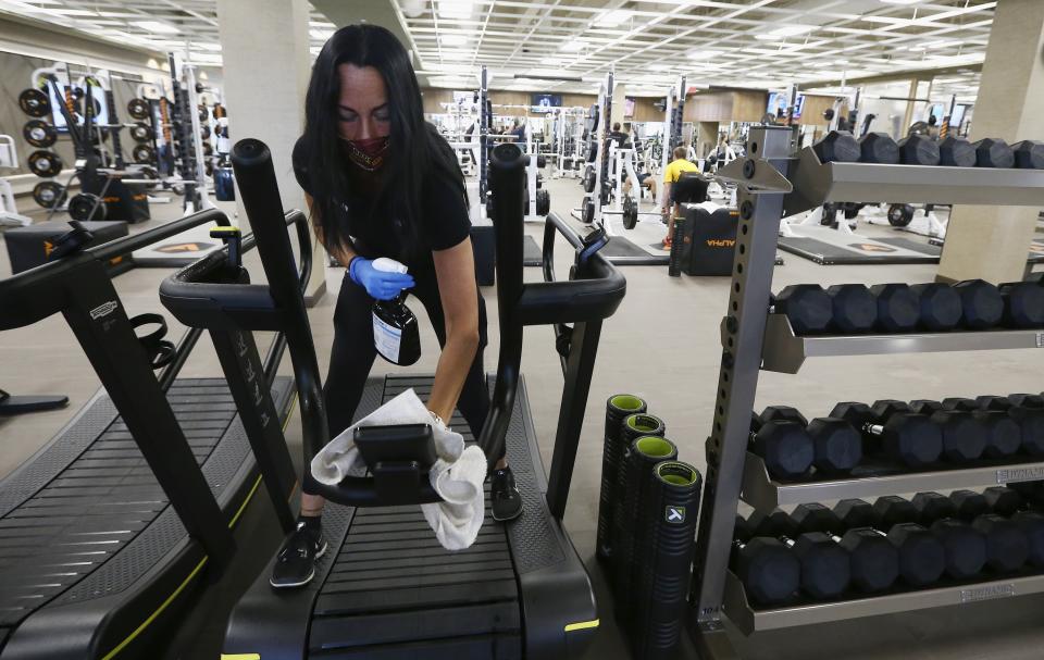 Jennifer McKeon, facilities operations national manager, disinfects equipment at the Life Time Biltmore as it opens for business after being closed due to the coronavirus Monday, May 18, 2020, in Phoenix. Big-box gyms and local fitness studios are reopening under a patchwork of protocols based on state and local guidance, but most are following these basics: spacing out cardio machines, touchless entry, smaller class sizes, increased cleaning and requiring users to clean all equipment before and after each use. (AP Photo/Ross D. Franklin)