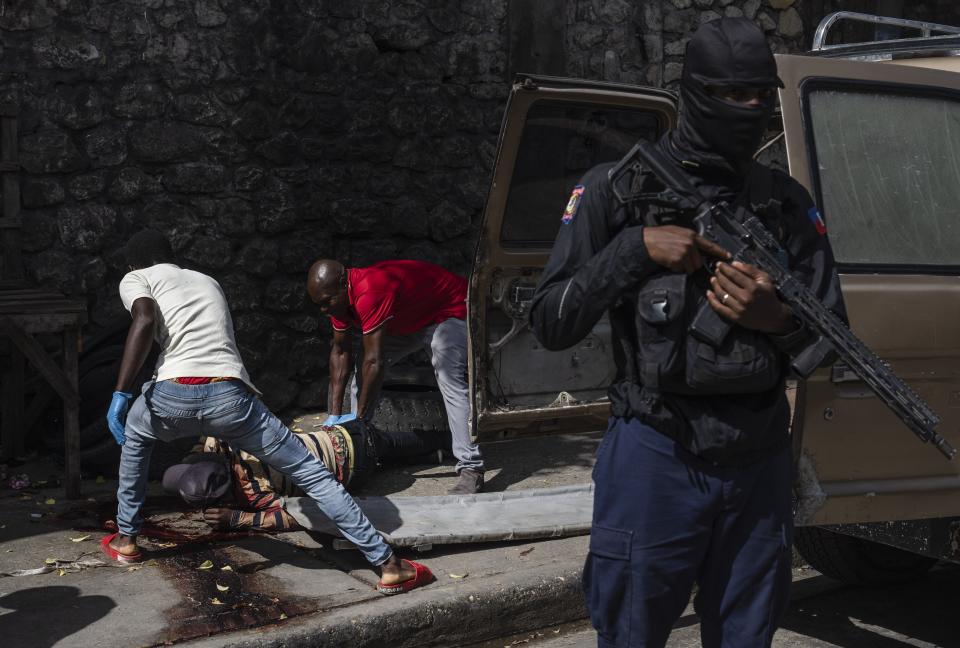 A police officer stands guard as forensic workers remove a bloodied body from the sidewalk in Port-au-Prince, Haiti, Wednesday, May 1, 2024. The forensic workers said the body had gunshot wounds. (AP Photo/Ramon Espinosa)