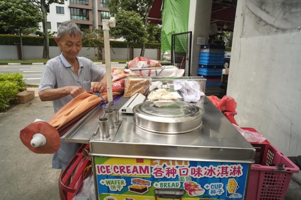 An elderly man securing a giant umbrella onto his ice cream cart.