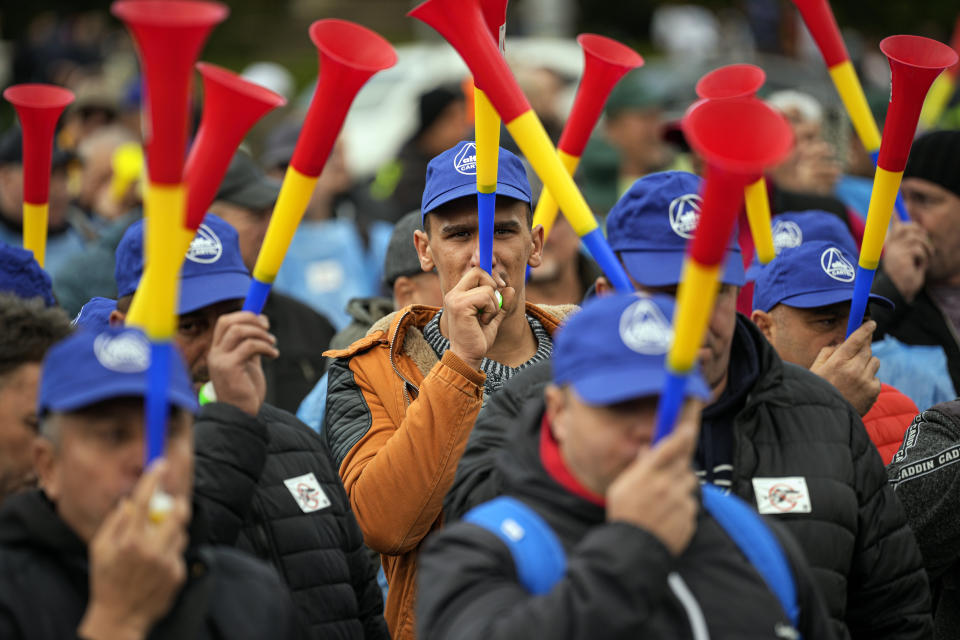 Trade union members blow horns during a protest outside the government headquarters in Bucharest, Romania, Thursday, Oct. 20, 2022. People joined a protest dubbed "The Anti-Poverty March" demanding salary and pensions increases and government controlled prices for energy and other basic commodities. (AP Photo/Andreea Alexandru)