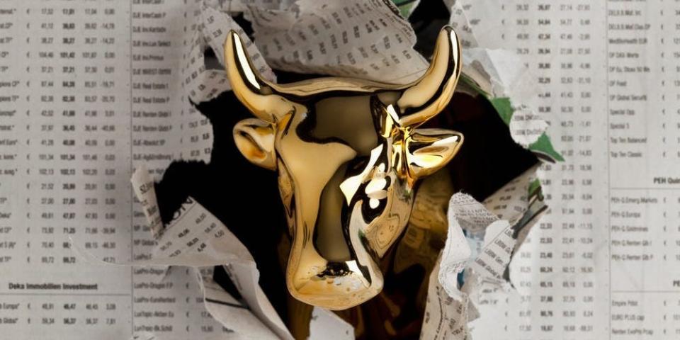 Gold bull emerging through newspaper