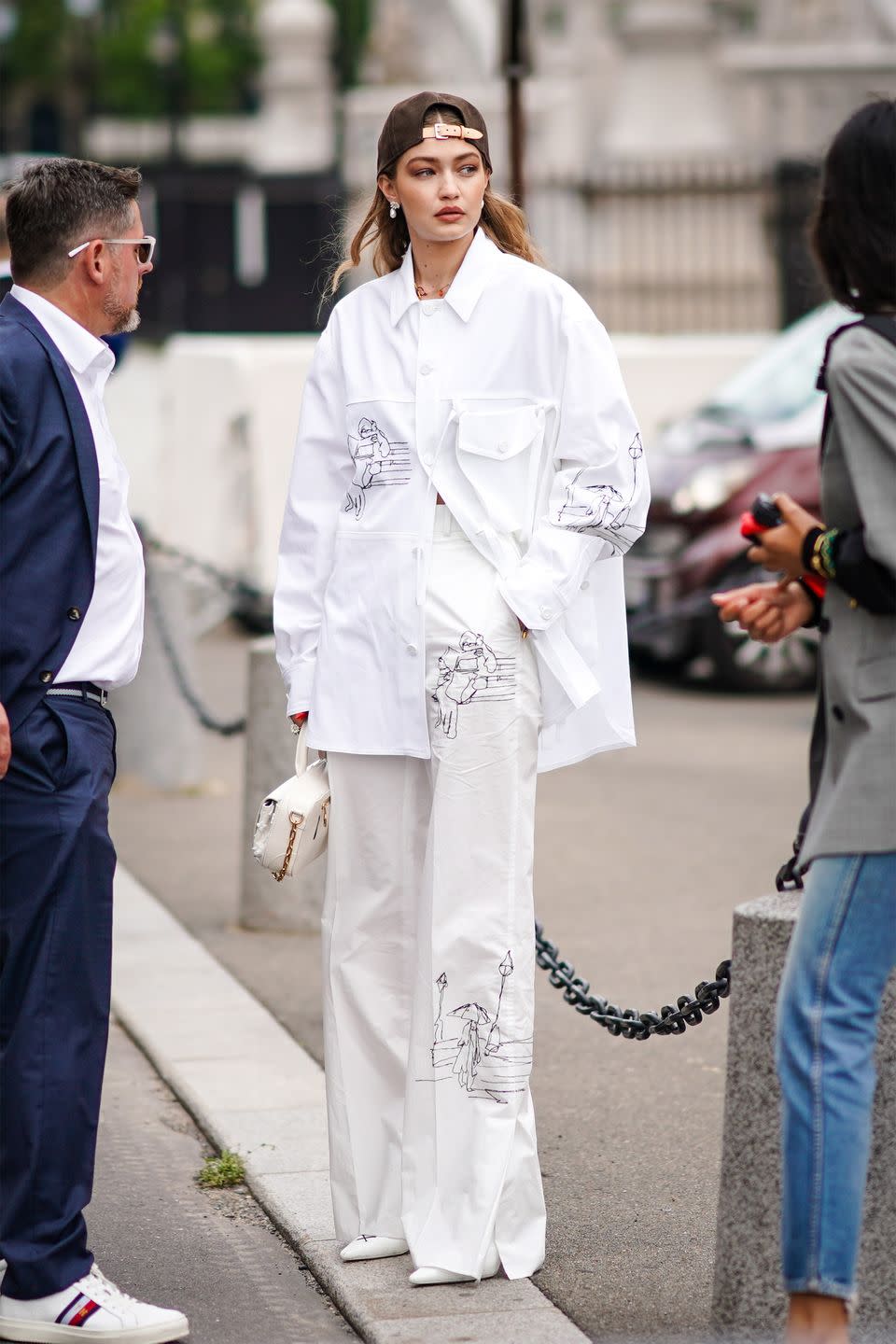 <p>In a brown cap, oversized white button-up, white wide-leg trousers and pointed white shoes.</p>
