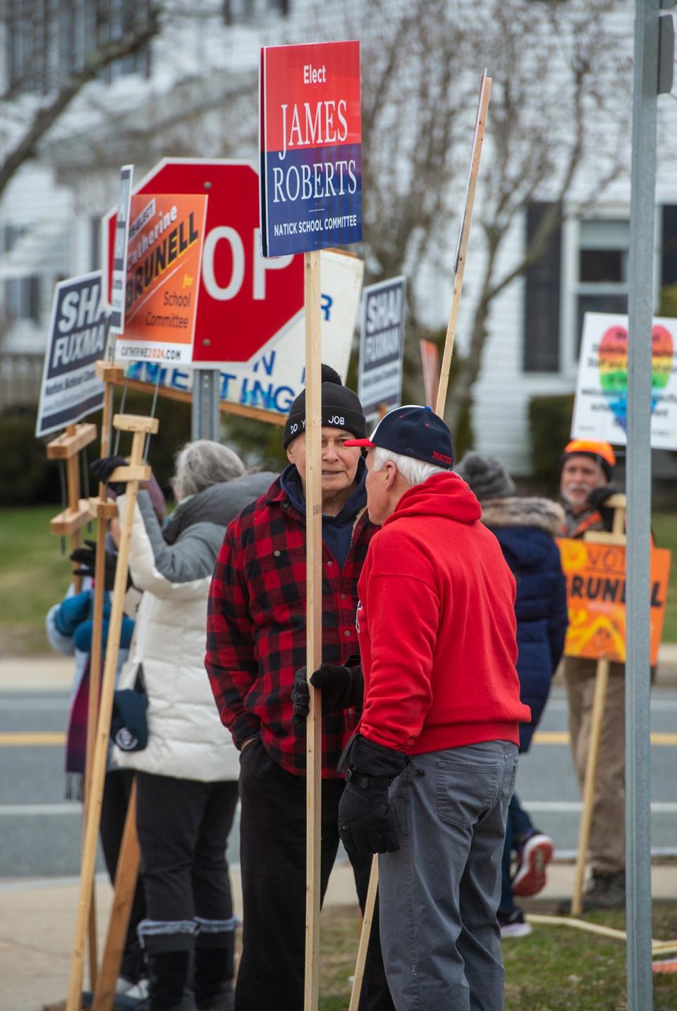 Candidates and others hold signs supporting various candidates outside the Natick Community Senior Center voting place during Tuesday's annual town election, March 26, 2024.