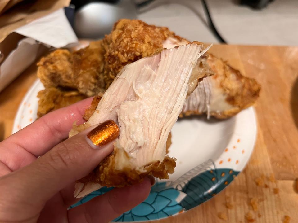 Hand holding piece of Safeway's chicken in front of white and blue plate