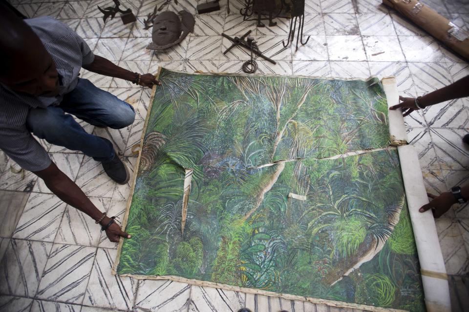In this May 29, 2019 photo, Clautaire Leveille with the help of a worker, rolls up an earthquake damaged painting by Haitian artist Jean-Claude Toussaint, at the Musée d'Art du Collège Saint Pierre, in Port-au-Prince, Haiti. The painting depicting a lush jungle scene has nearly been ripped in half and also slashed diagonally. It remains rolled up with yellowed masking tape that has lost its stickiness. (AP Photo/Dieu Nalio Chery)