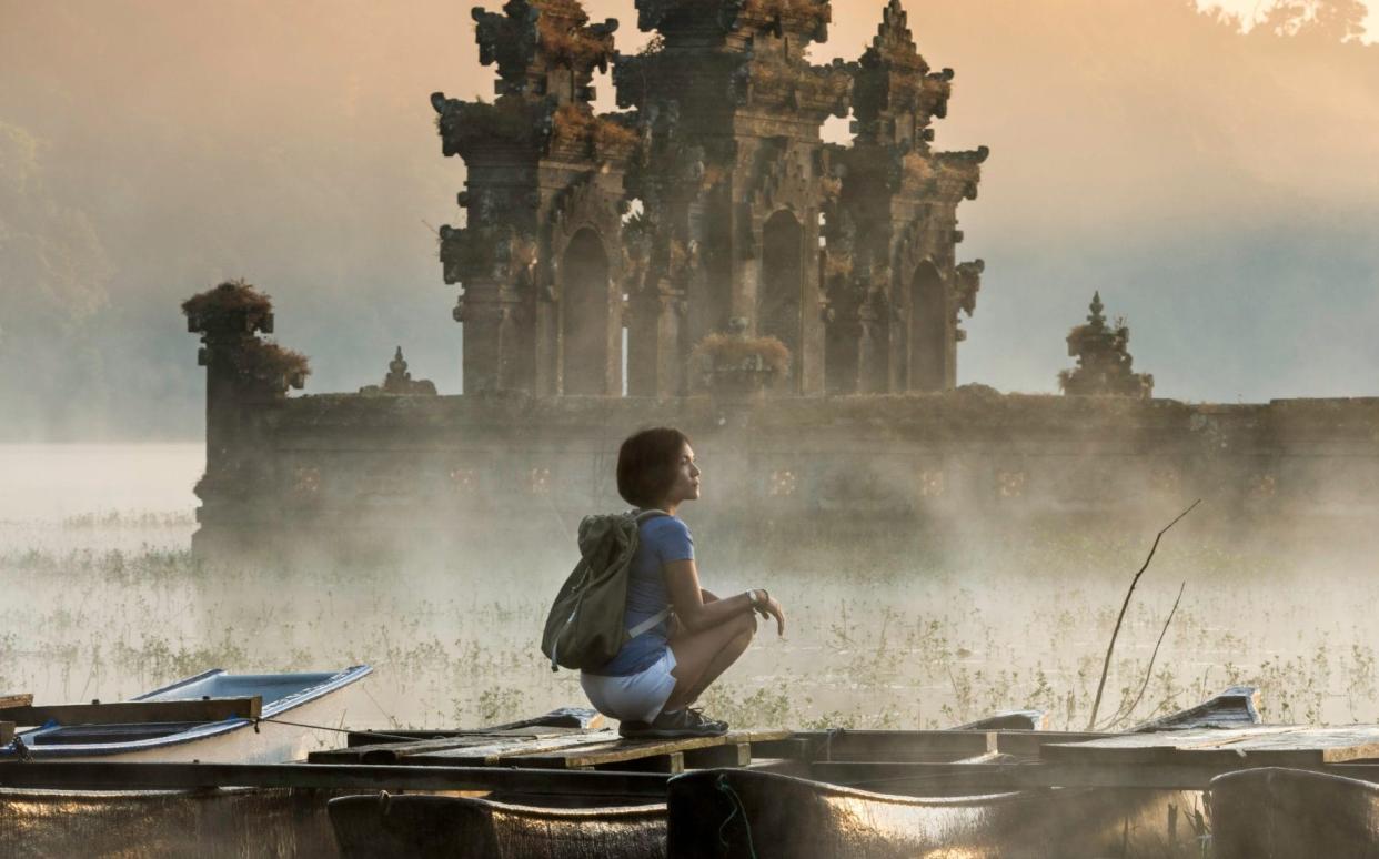 Asia, Indonesia, Bali, young Asian woman sitting on boat admiring Tamblingan temple - Stone RF/Getty