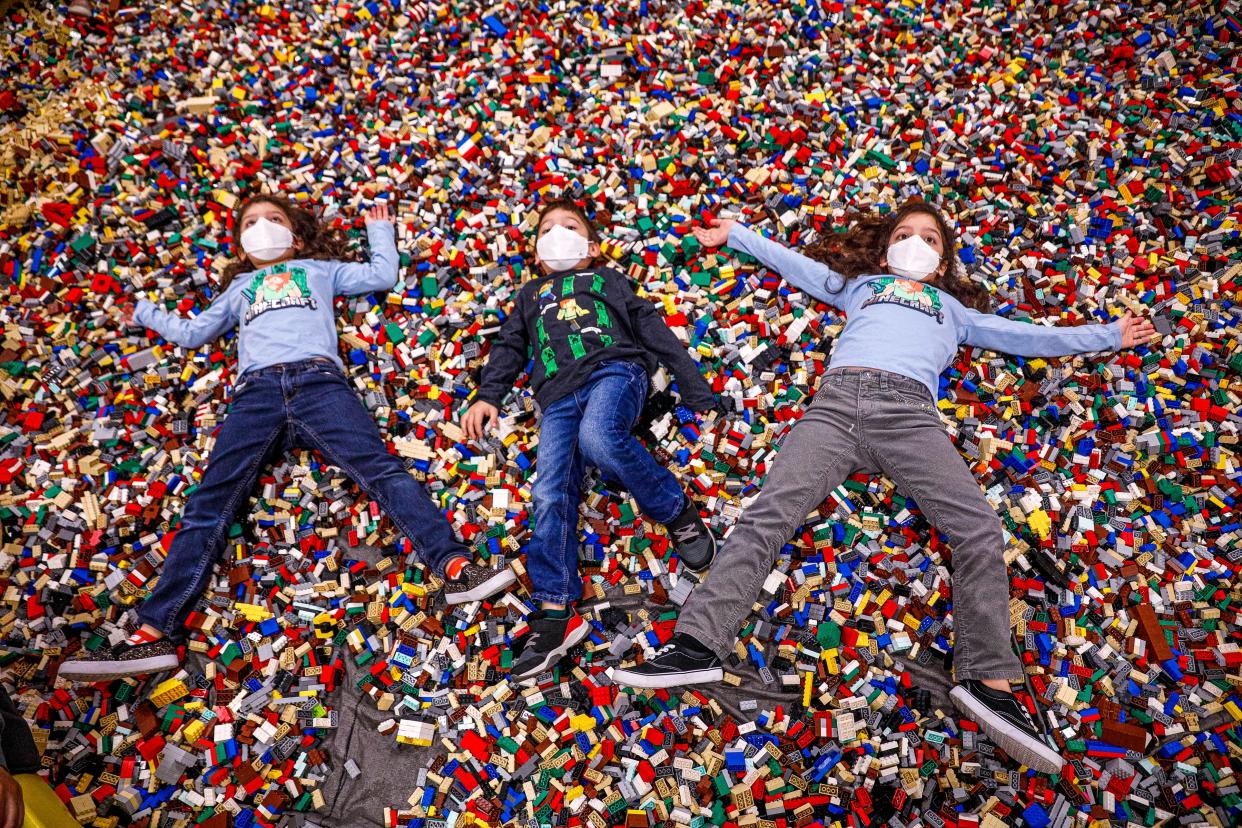 From left to right, siblings Emme, Aidan, and Mia Guerra lie down in a pool of plastic bricks at Brick Fest Live at the Palmer Events Center in Austin, Texas on Jan. 1, 2022.