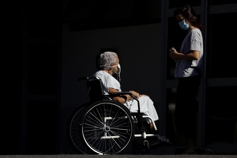 Acompañada por su nieta, Elizabeth Nader, de 74 años, espera a una ambulancia para ser trasladada a una unidad de terapia para pacientes con COVID-19 en la entrada de urgencias del hospital público HRAN de Brasilia, Brasil, el 16 de abril de 2021. (AP Foto/Eraldo Peres)