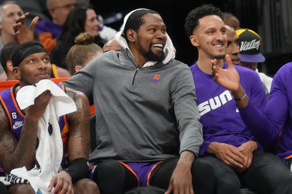 Phoenix Suns forward Kevin Durant, center, jokes around with teammates Torrey Craig, left, and Landry Shamet on the bench as they play a game against the Denver Nuggets at Footprint Center in Phoenix on March 31, 2023.