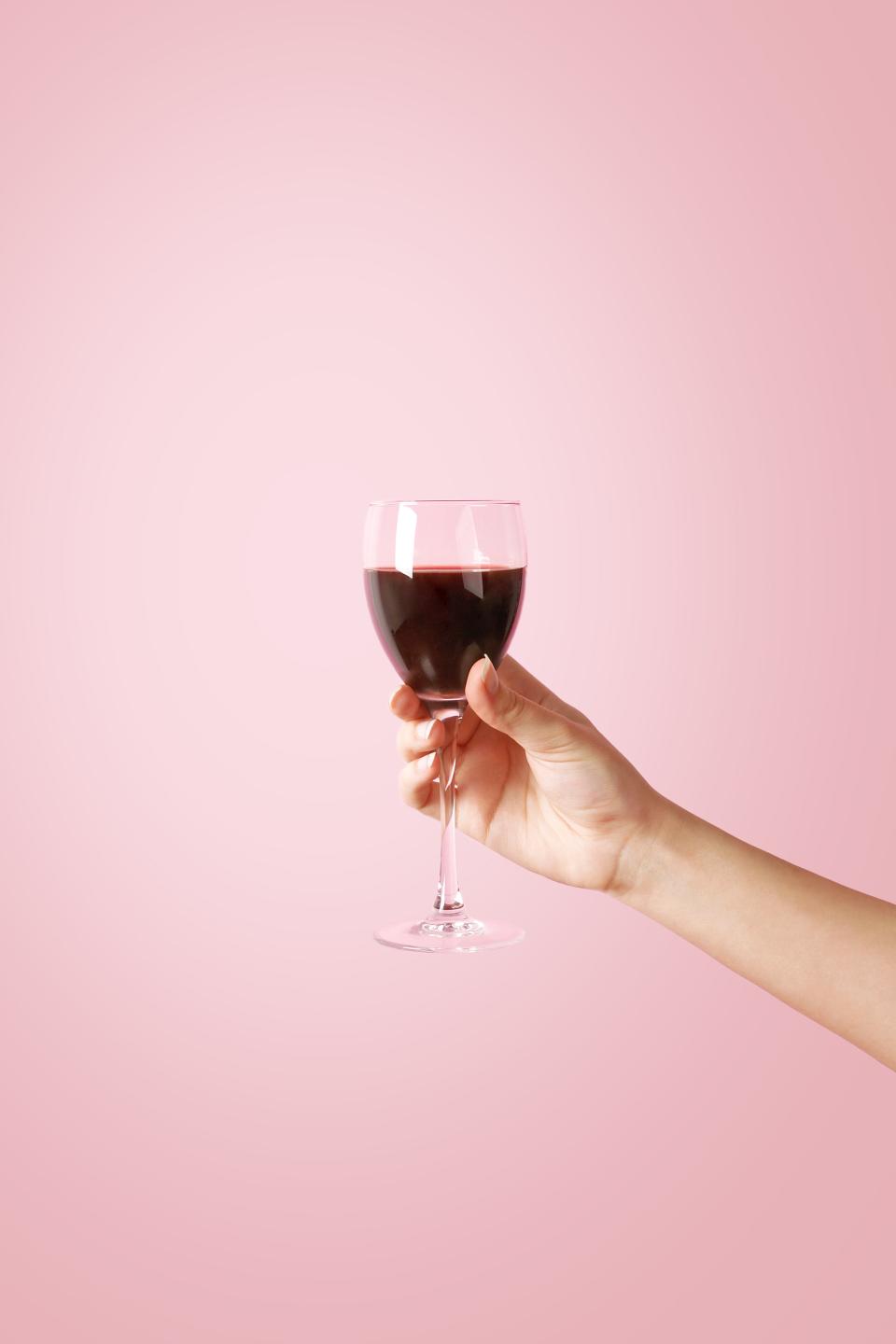 Red wine glass held against a pink background.