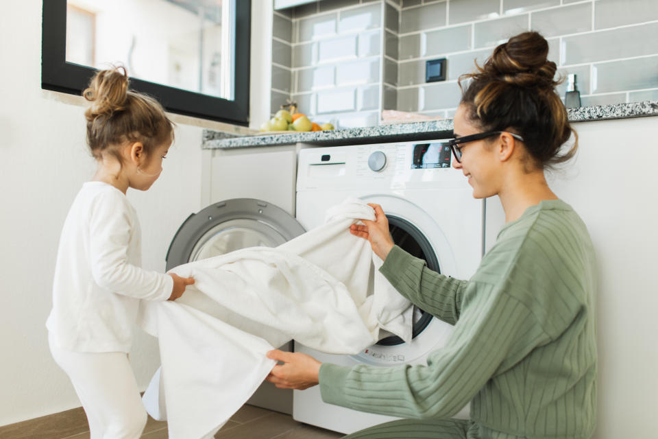 Mutter und kleines Mädchen sind mit der Wäsche vor einer Waschmaschine beschäftigt. (Bild: Getty Images) 