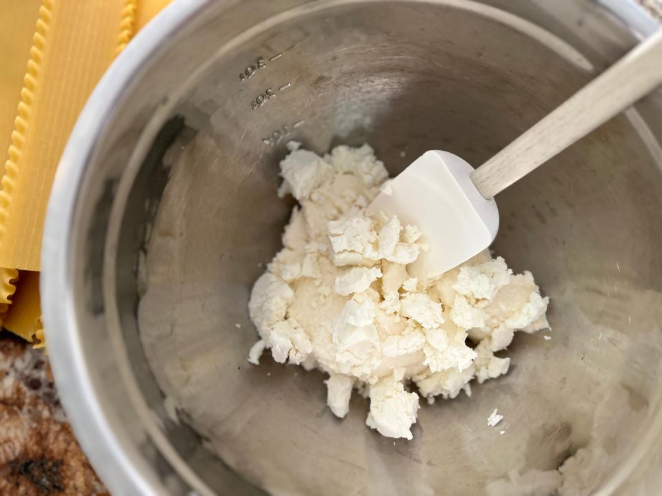 ricotta and goat cheese in a metal mixing bowl with a rubber spatula