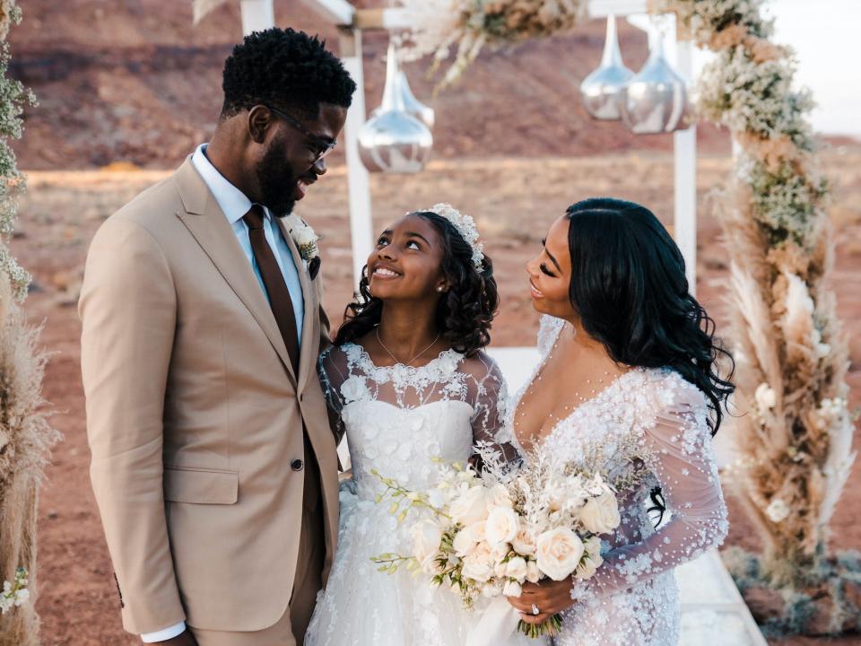 A bride and groom look at their daughter who smiles at the groom.