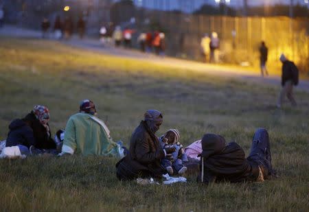 A migrant mother holds her child as she sits on the grass with other migrants at nightfall in Coquelles, near Calais, France, July 30, 2015. REUTERS/Pascal Rossignol