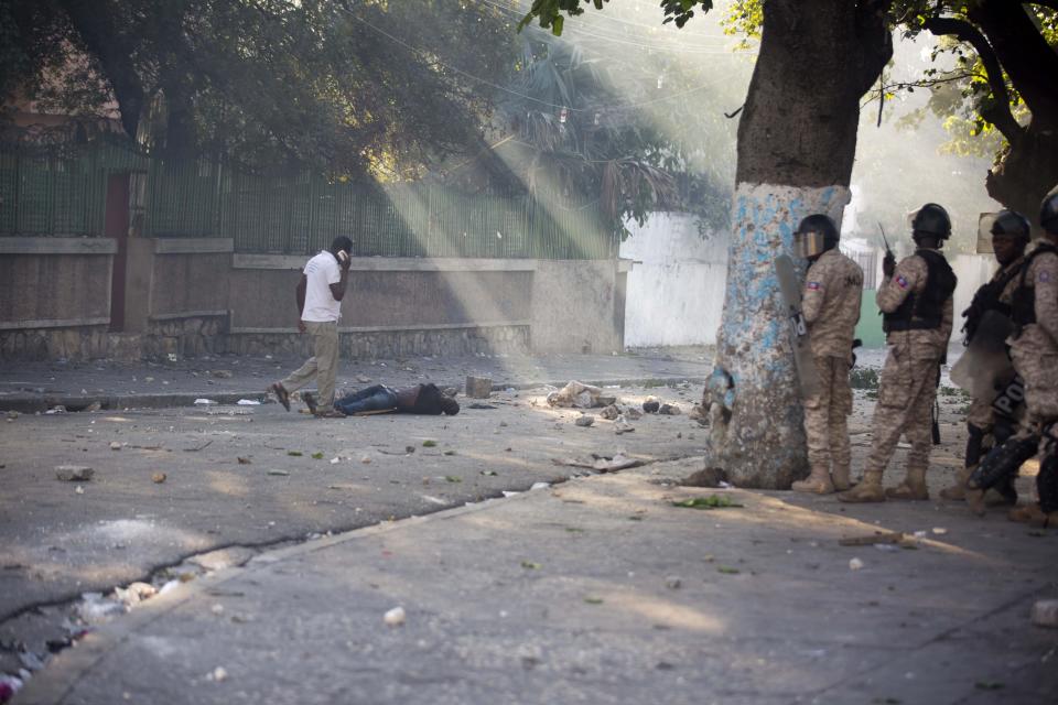Police officers stand near the body of a person killed during the violent clashes between the police and demonstrators near the national palace, during a protest to demand the resignation of President Jovenel Moise and demanding to know how Petro Caribe funds have been used by the current and past administrations, in Port-au-Prince, Haiti, Saturday, Feb. 9, 2019. ( AP Photo/Dieu Nalio Chery)