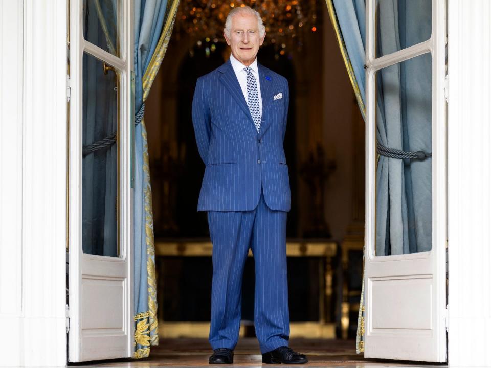 King Charles stands in front of an open door frame.