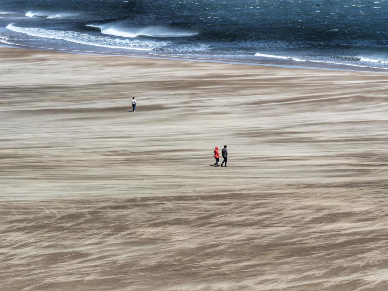 Strong winds whip up the sand as people walk along Tynemouth beach on the north east coast: PA