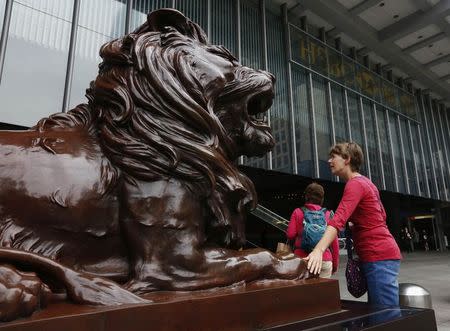 A woman touches "Stephen", one of the two bronze lion sculptures by W.W. Wagstaff commissioned in 1935, outside HSBC headquarters in Hong Kong March 3, 2015. REUTERS/Bobby Yip