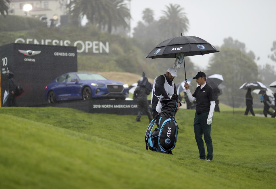 Jordan Spieth holds an umbrella for his caddie, Michael Greller, on the 10th hole before play was suspended during the first round of the Genesis Open golf tournament at Riviera Country Club Thursday, Feb. 14, 2019, in the Pacific Palisades area of Los Angeles. (AP Photo/Ryan Kang)