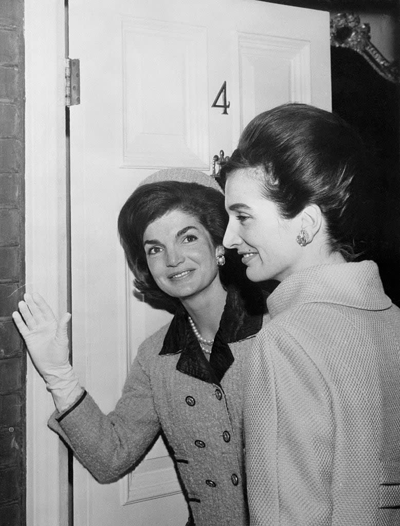 Jaqueline Kennedy and Lee Radziwill are photographed at the door of a house, both dressed in elegant and stylish coats