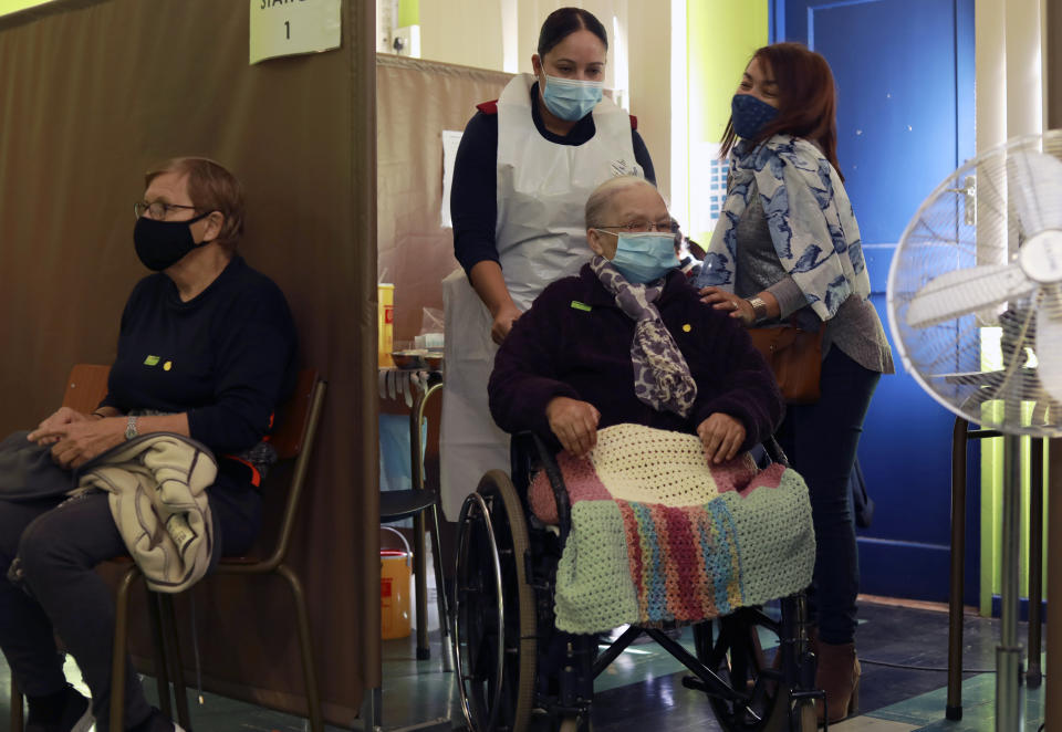 FILE - In this June 11, 2021, file photo, Catherine Daries, 87, in a wheelchair, is helped after receiving a first dose of the Pfizer COVID-19 vaccine at a vaccination center, at the Karl Bremer Hospital, in Cape Town, South Africa. New infections in South Africa rose to record levels in recent days, part of a rapid rise across the continent, and experts say the surge here has not yet peaked. South Africa reimposed several restrictions, and its vaccination drive is finding its feet after several stumbles. But even as the campaign gathers pace, experts say it's too late to reduce the deadly impact of the current spike. (AP Photo/Nardus Engelbrecht, File)