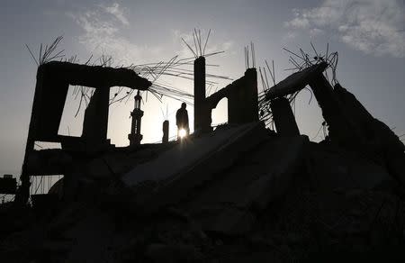 A Palestinian man walks atop the remains of a house, that witnesses said was destroyed by Israeli shelling during a 50-day war last summer, in Khan Younis in the southern Gaza Strip, March 10, 2015. REUTERS/Ibraheem Abu Mustafa