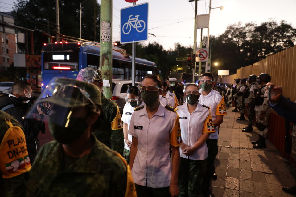 Medical workers stand outside the General Hospital as they wait to get vaccinated for COVID-19, as military forces stand guard in Mexico City, early Thursday, Dec. 24, 2020. The first batches of vaccines produced by Pfizer and its German partner, BioNTech arrived the previous day. (AP Photo/Eduardo Verdugo)