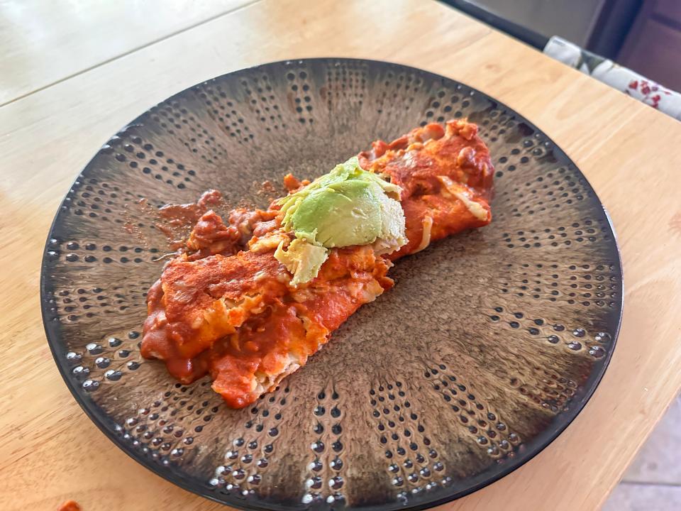 A brown plate with two enchiladas stacked on top of each other with a mound of avocado on top