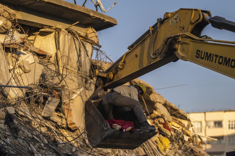 Un hombre sostiene un cadáver mientras una retroexcavadora los aparta de un edificio colapsado en Kahramanmaras, en el sureste de Turquía, el jueves 9 de febrero de 2023. (AP Foto/Petros Giannakouris)