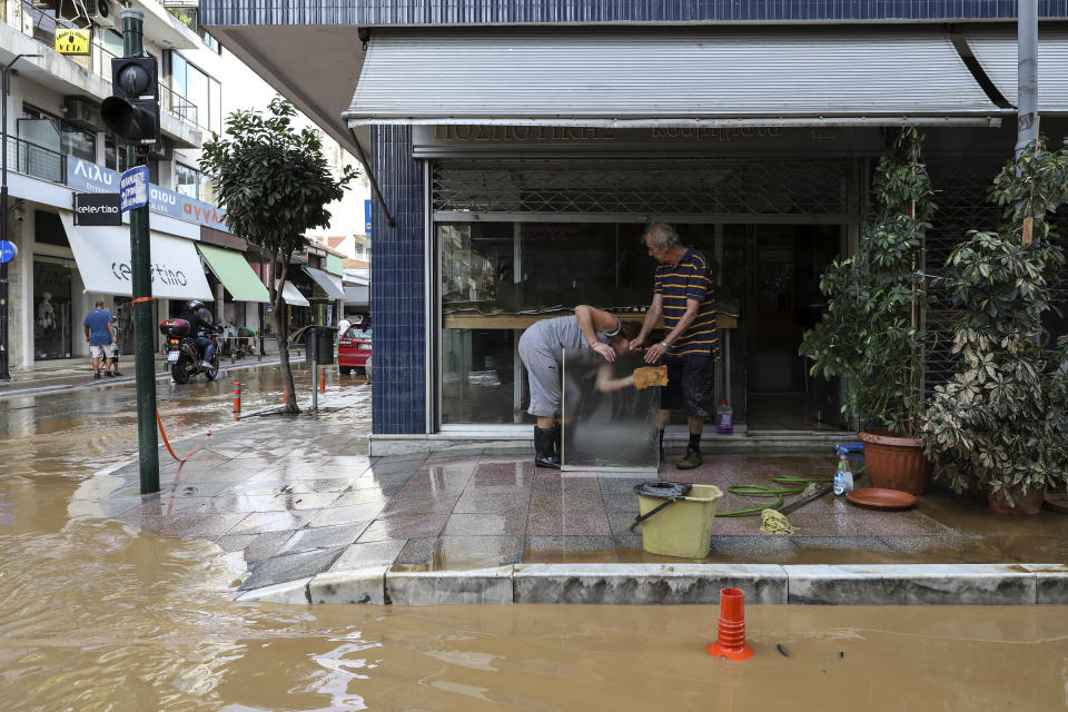 Residents clean a sheet of glass next to a flooded street after a storm at Karditsa town, Saturday, Sept. 19, 2020. Two people have died and one is reported missing in the central Greek region of Thessaly as a rainstorm pounded parts of central and western Greece overninght and caused rivers to burst their banks and flood surrounding areas. (AP Photo/Vaggelis Kousioras)